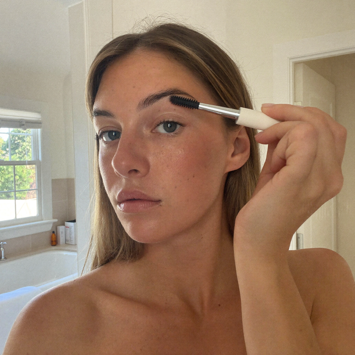 A woman brushing colour through her eyebrow with an angled brow brush